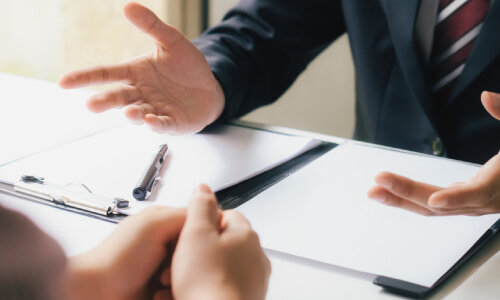attorneys hands talking to someone across a desk with papers and a pen on the table patents