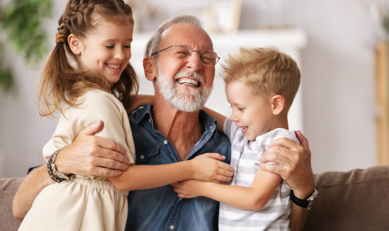 Cheerful aged man smiling and embracing grandkids while resting on couch at home together