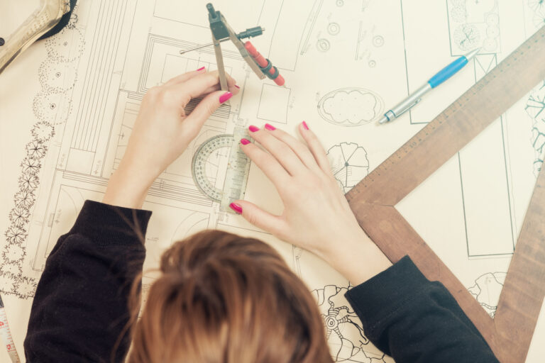 Architect drawing on a blueprint with a compass and ruler.