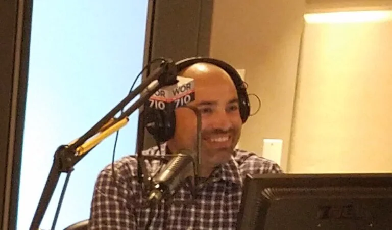 Man in a radio studio wearing headphones, speaking into a WOR 710 microphone.
