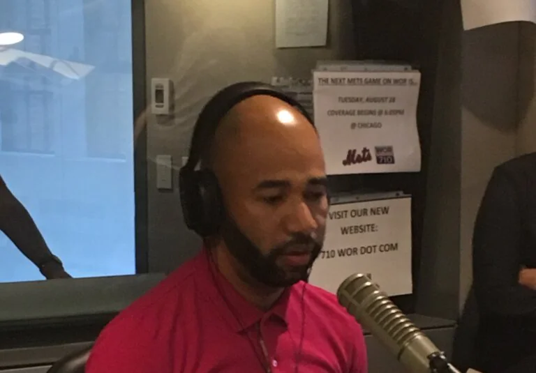 Man in a radio studio wearing headphones speaking into a microphone.