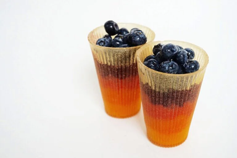 `Two colorful layered edible cups filled with fresh blueberries on a white background`