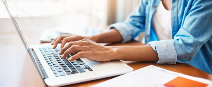 woman typing on a laptop with a paper on the desk patents