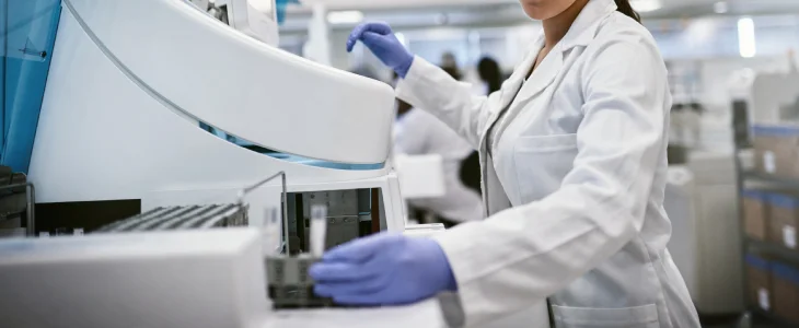 A scientist in a lab coat and gloves operates a large machine in a laboratory.