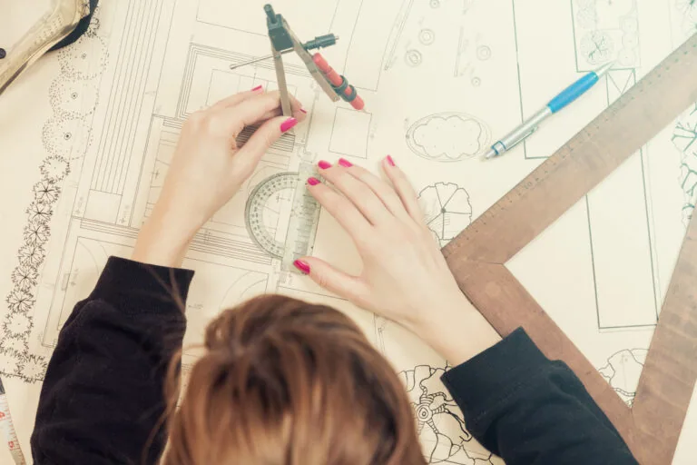 Architect drawing on a blueprint with a compass and ruler.